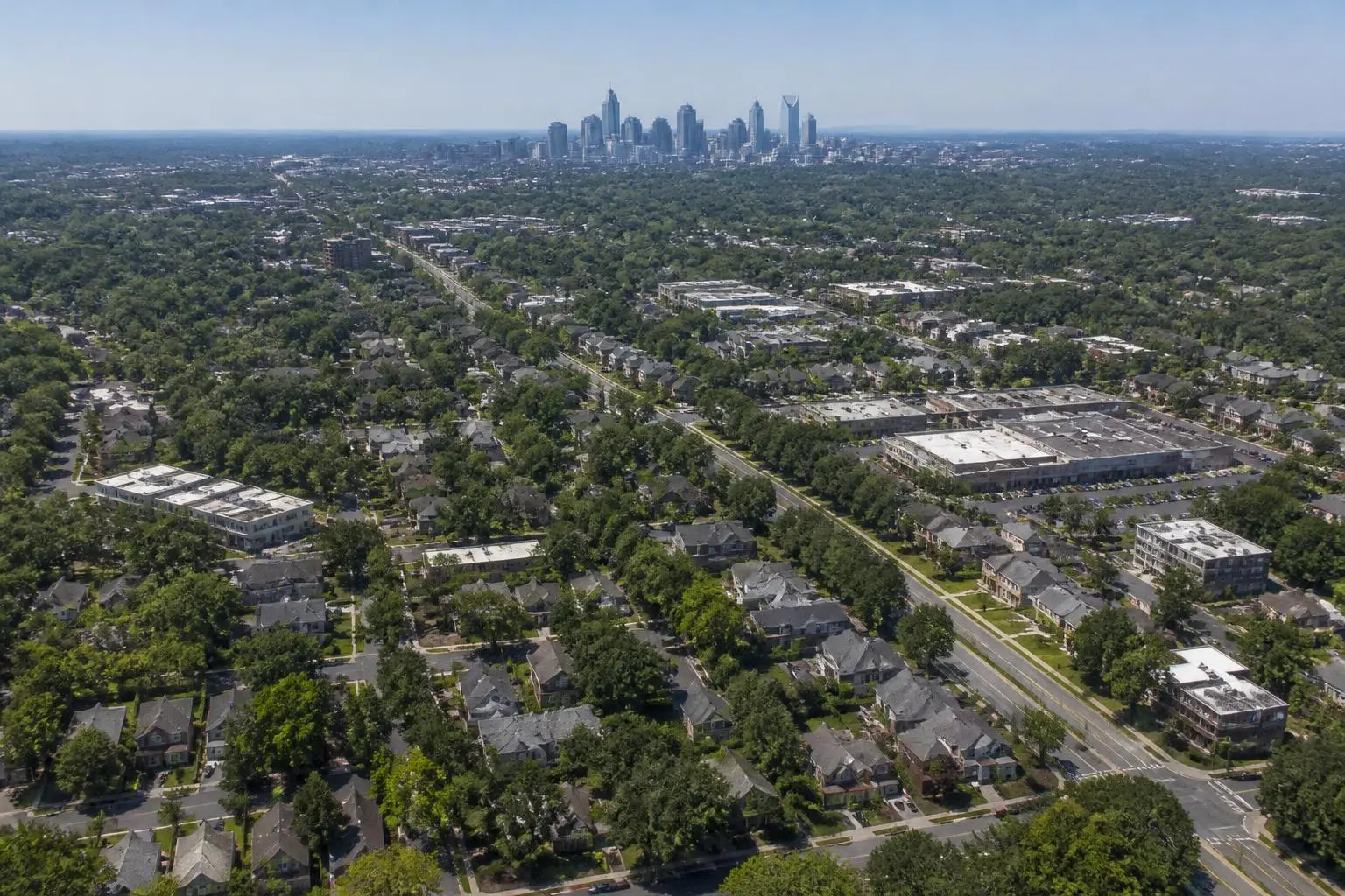 Aerial view of tree-covered Charlotte neighborhoods with the skyline beyond